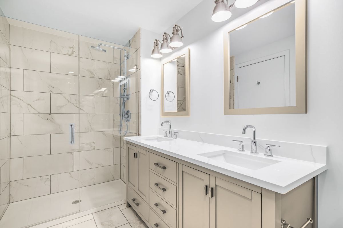 Bright bathroom with a glass walk-in shower, marble-look tile, and a double vanity