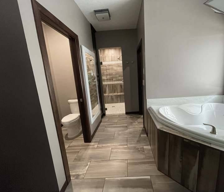 New construction master bathroom in Rockville, MN, with a hallway past the water closet and walk-in shower to the corner soaking tub